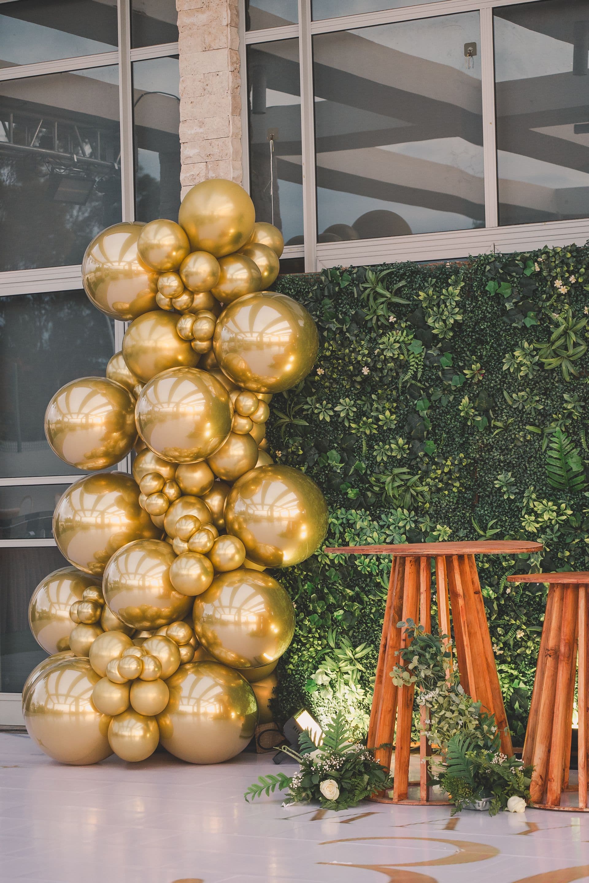 Elegant gold organic balloon garland installation styled against a lush greenery wall
