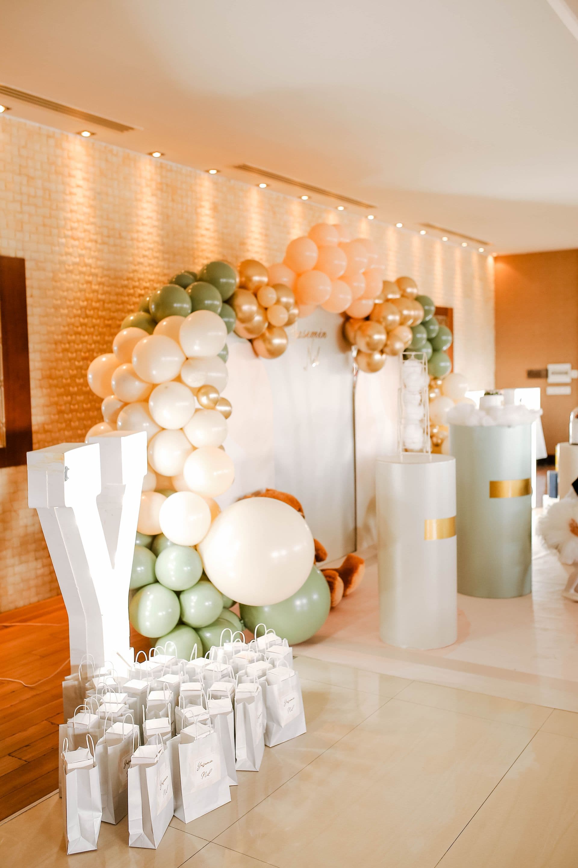 Sage green, cream, and gold organic balloon arch installation with an elegant step-and-repeat wall