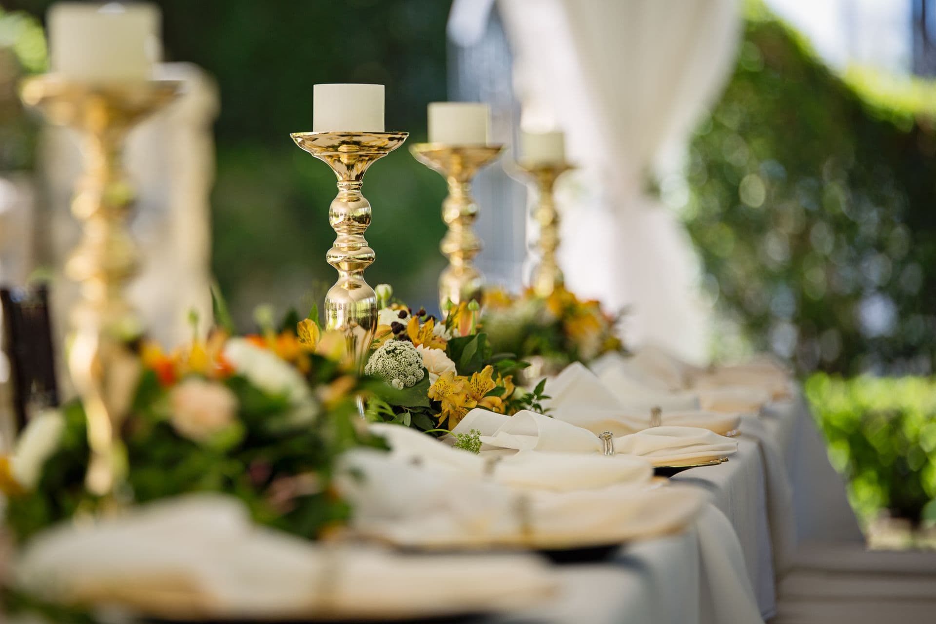Gold candelabras and floral table runner along an elegant outdoor wedding reception table